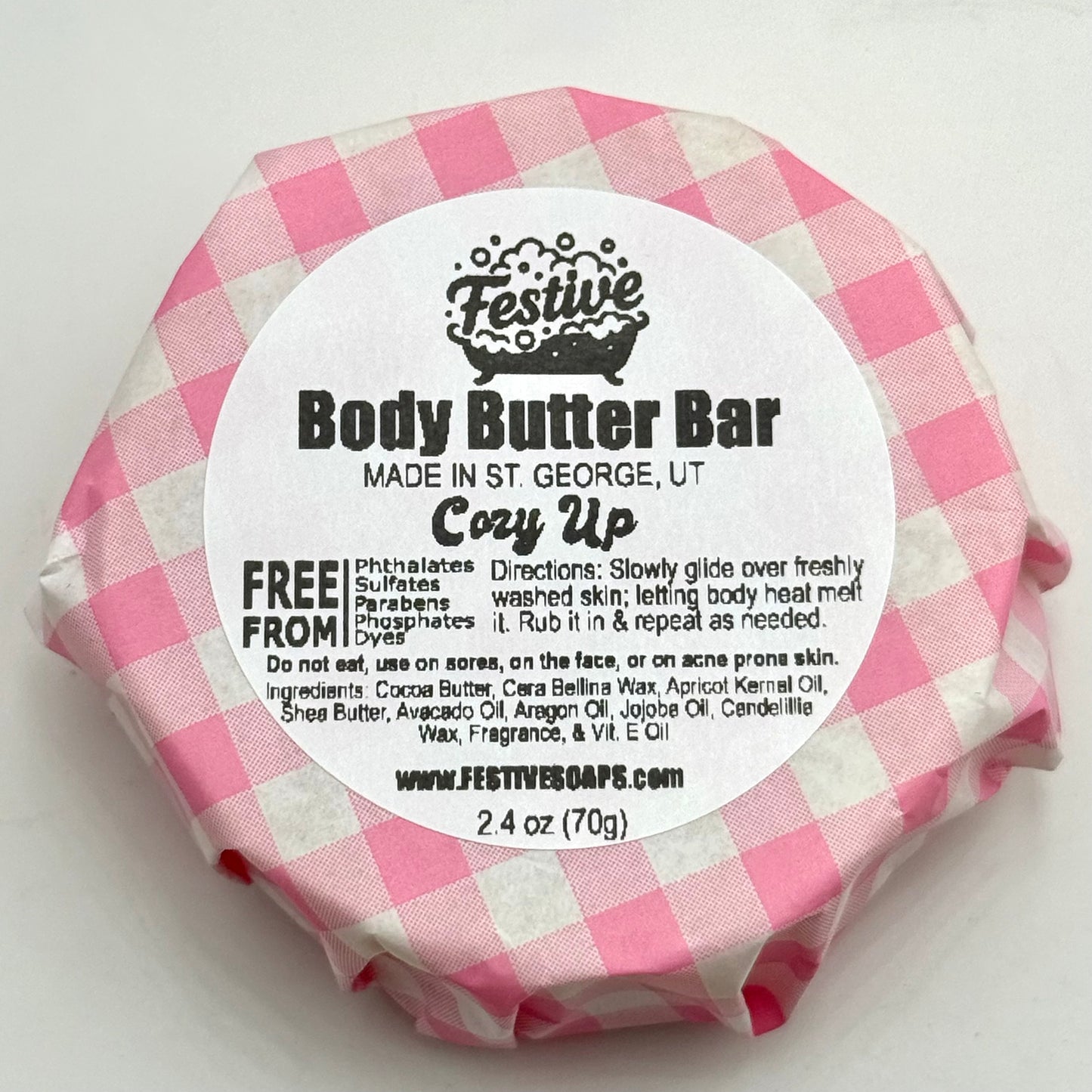Body butter bar wrapped in pink and white checkered paper with a label on a white background