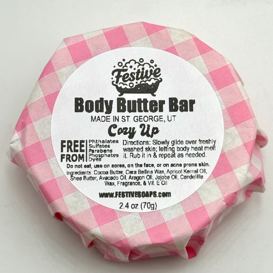 Body butter bar wrapped in pink and white checkered paper with a label on a white background