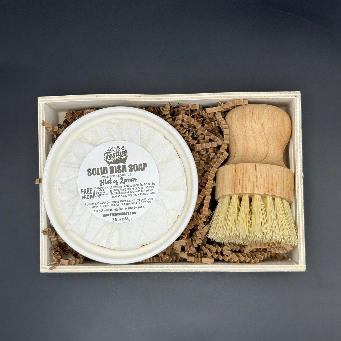 Solid dish soap and wooden brush set in a box on a dark background